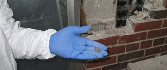 gloved hand holding sample of suspected asbestos found during home inspection